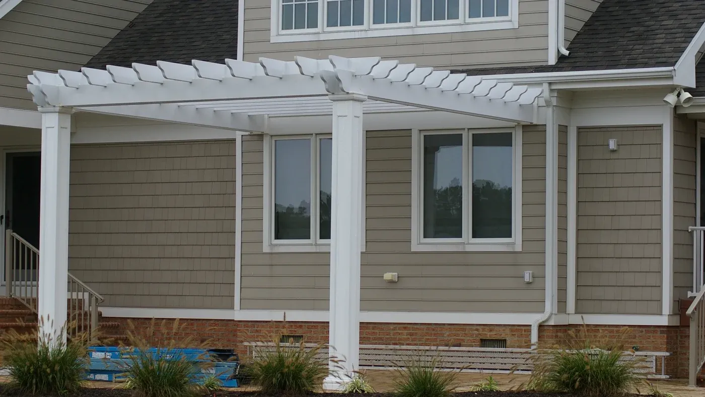 A tan-sided home with white trim and a white pergola over the patio area