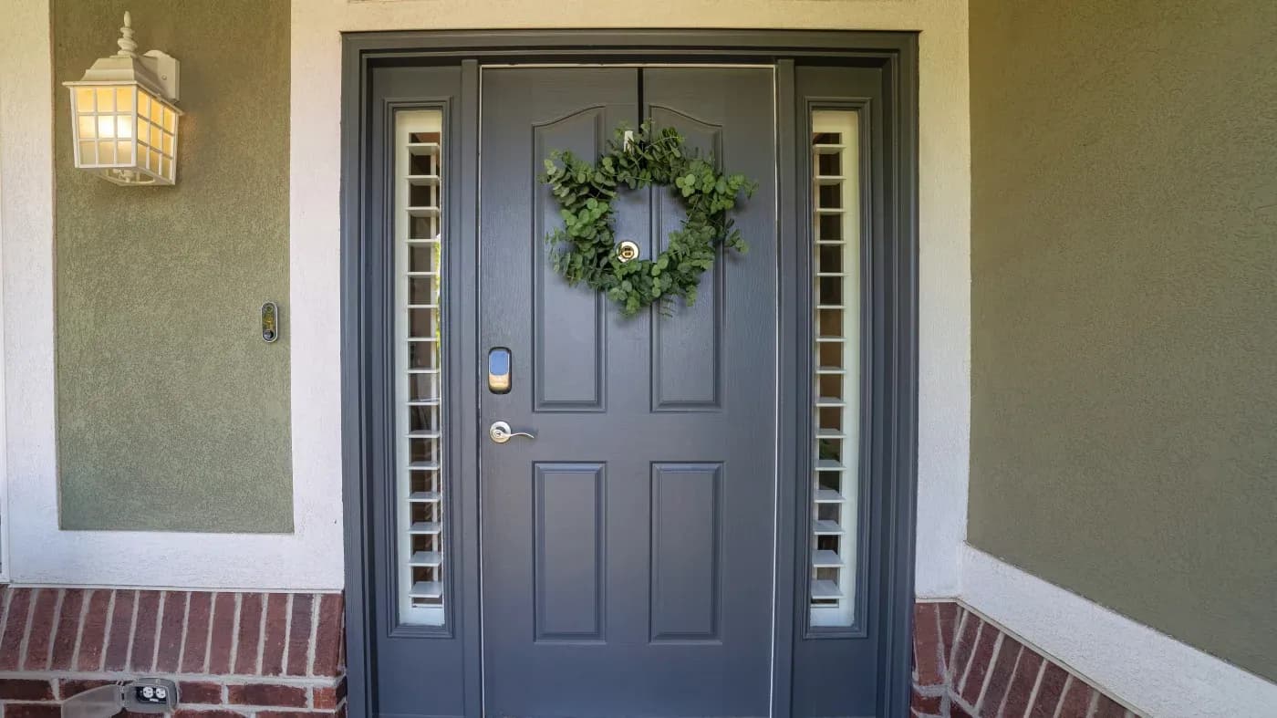 A black entry door with a green wreath and thin glass panes on either side