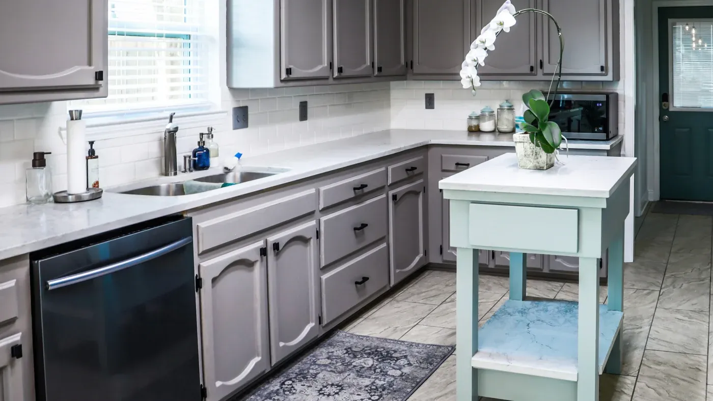 A kitchen with gray cabinets, white countertops, and a tile floor