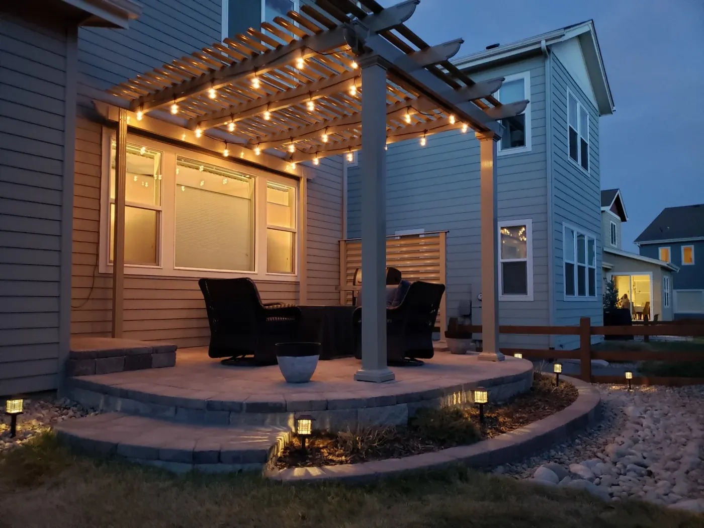 A pergola with lights on it above a patio with furniture