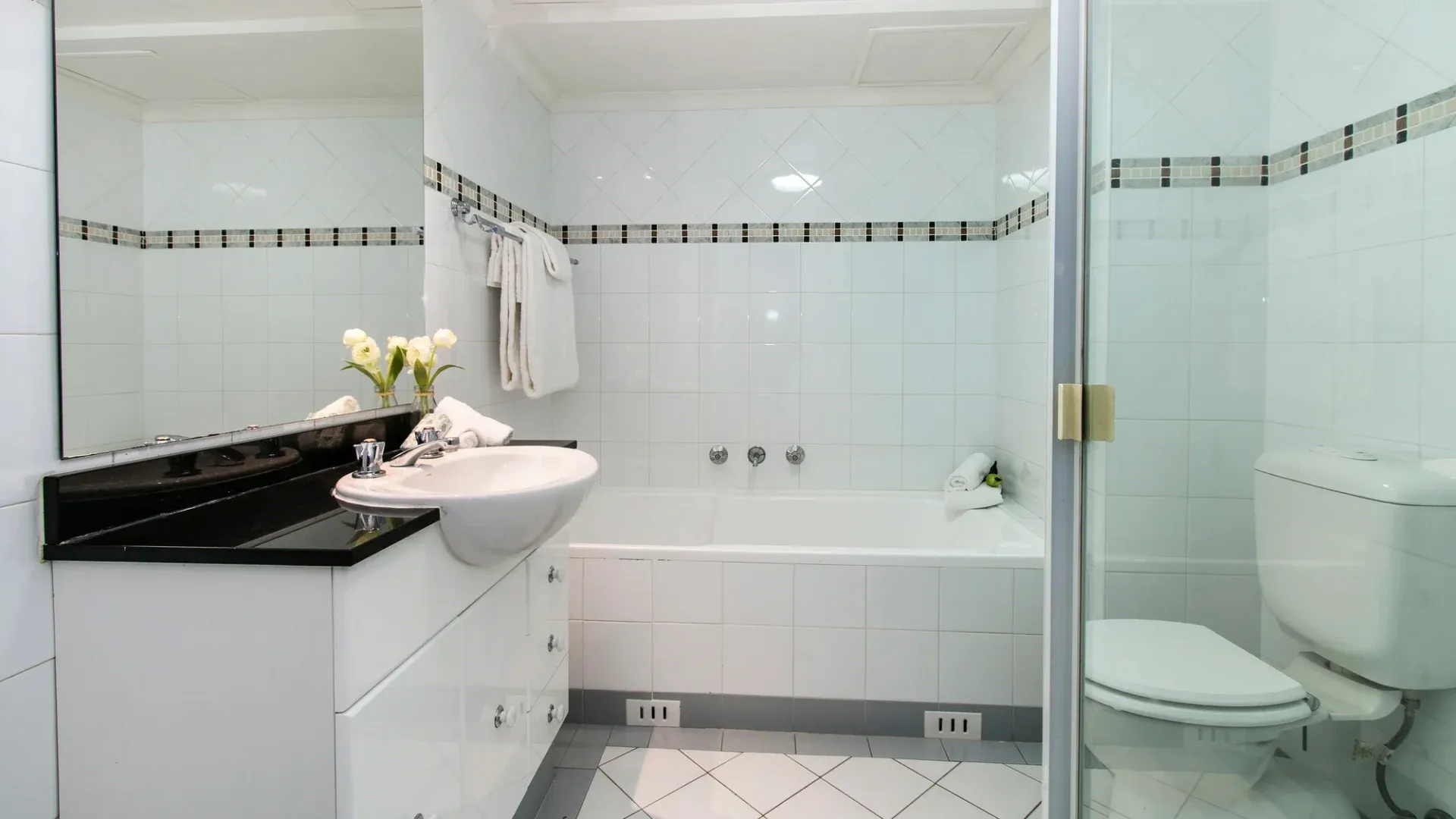 A white-themed bathroom with a large mirror and black countertop on the vanity