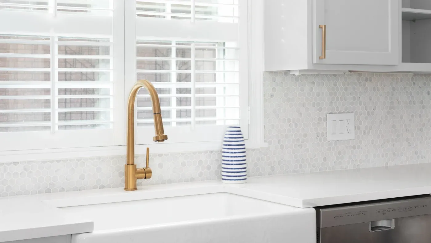 A kitchen with white countertops and a gold sink