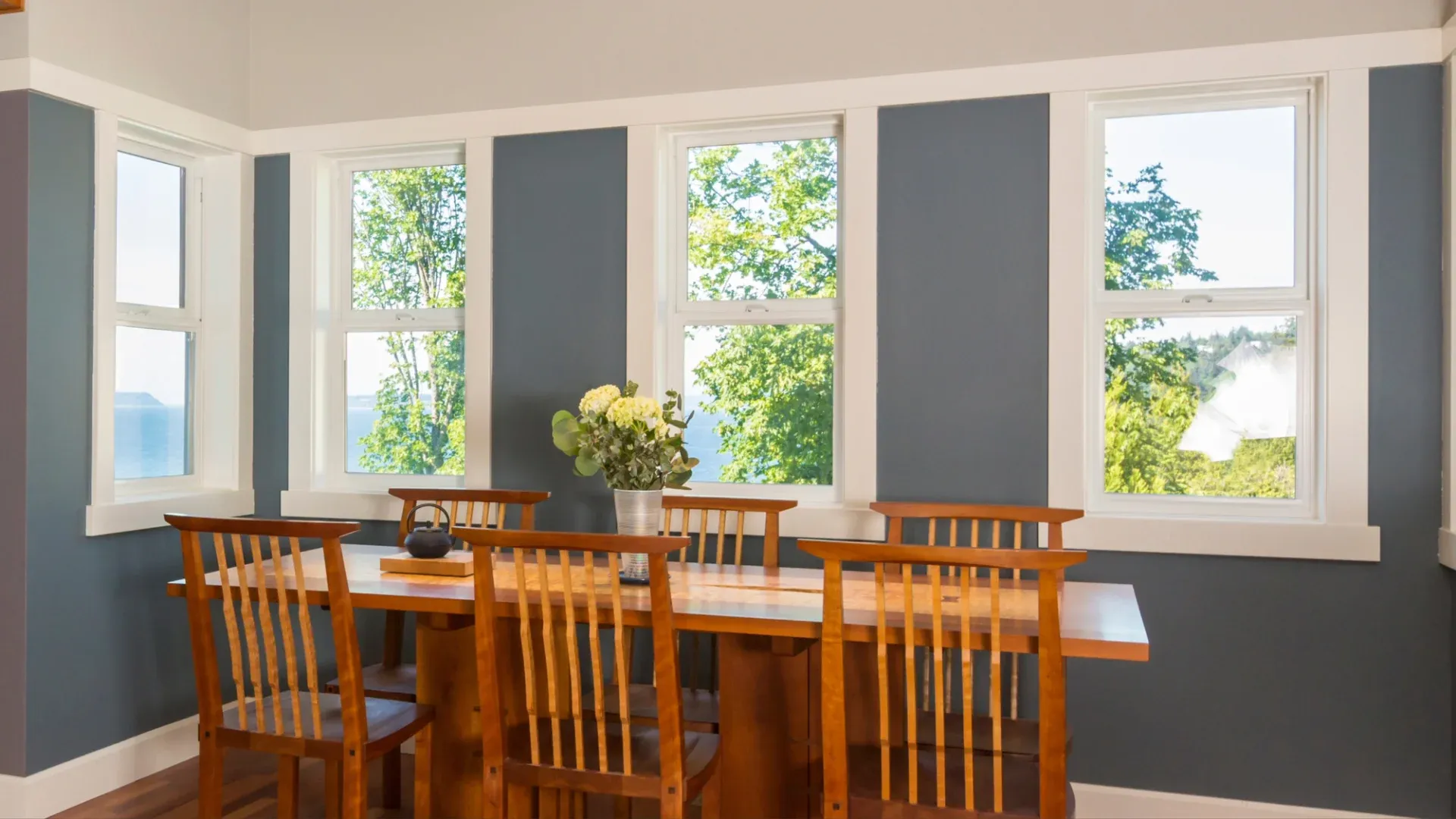 A dining room with a wood table, blue walls, and white windows