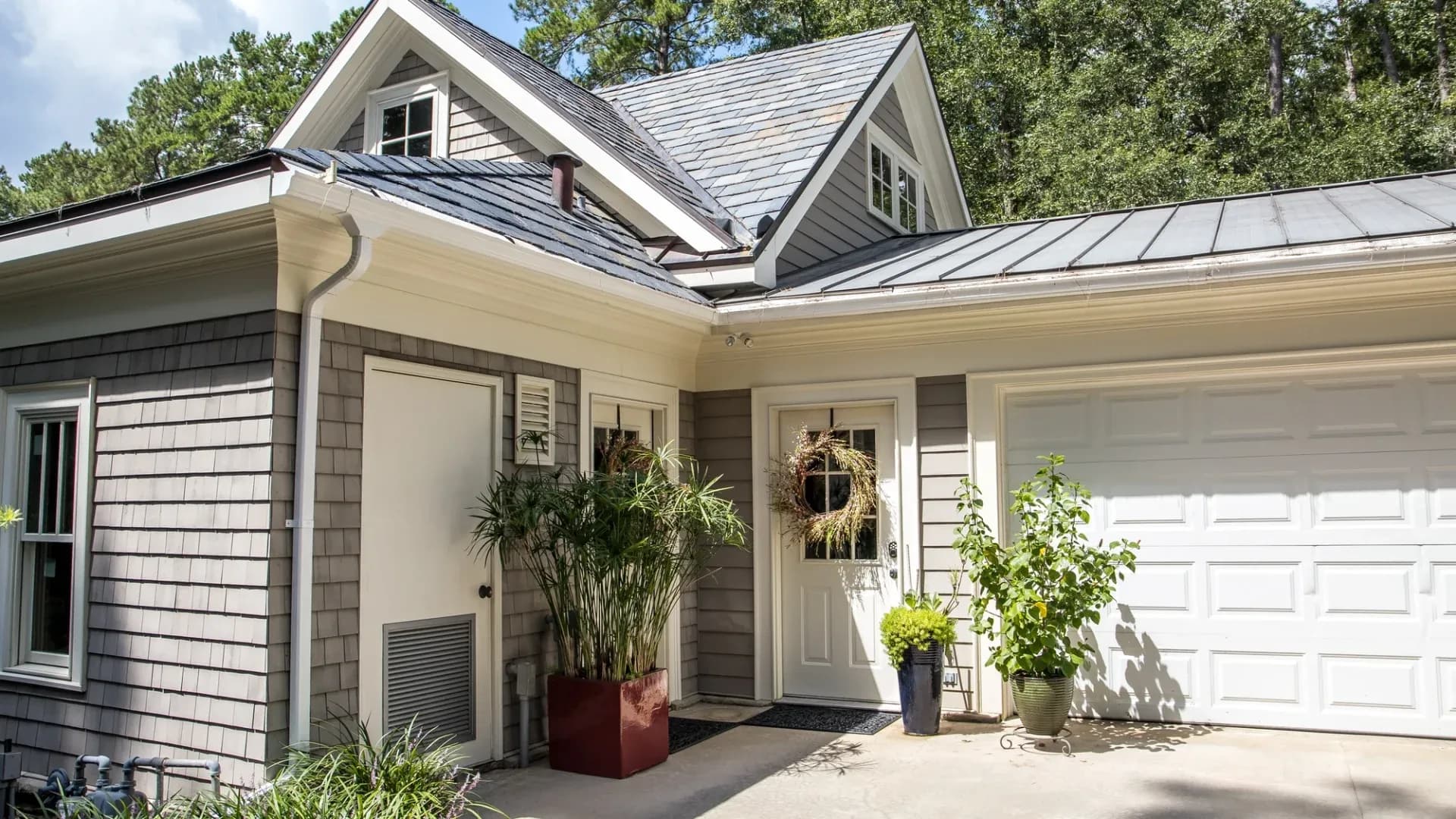 A small home with gray siding, a white entry door, and a white garage door
