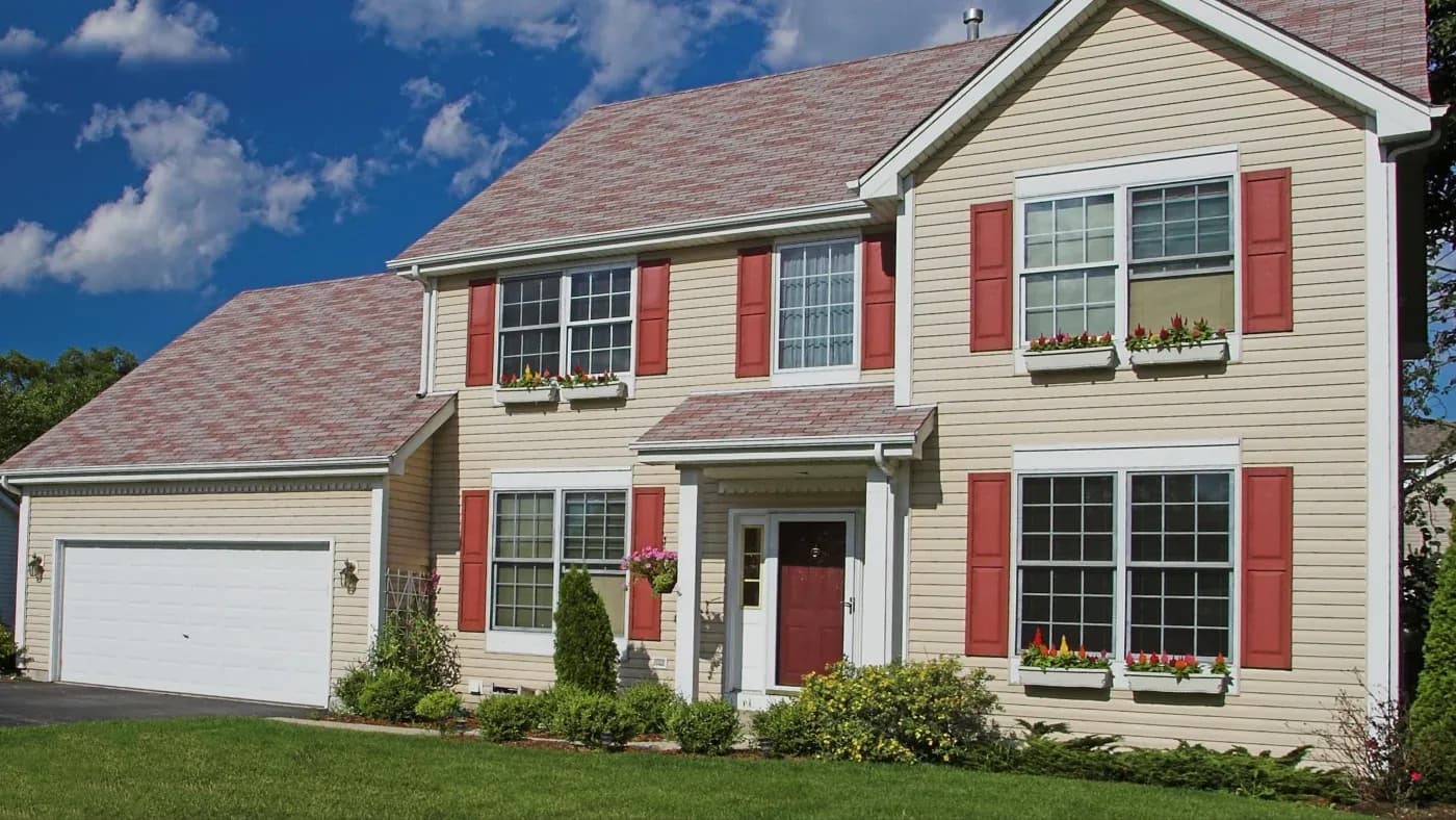 A home with beige siding, red shutters, and a brown roof