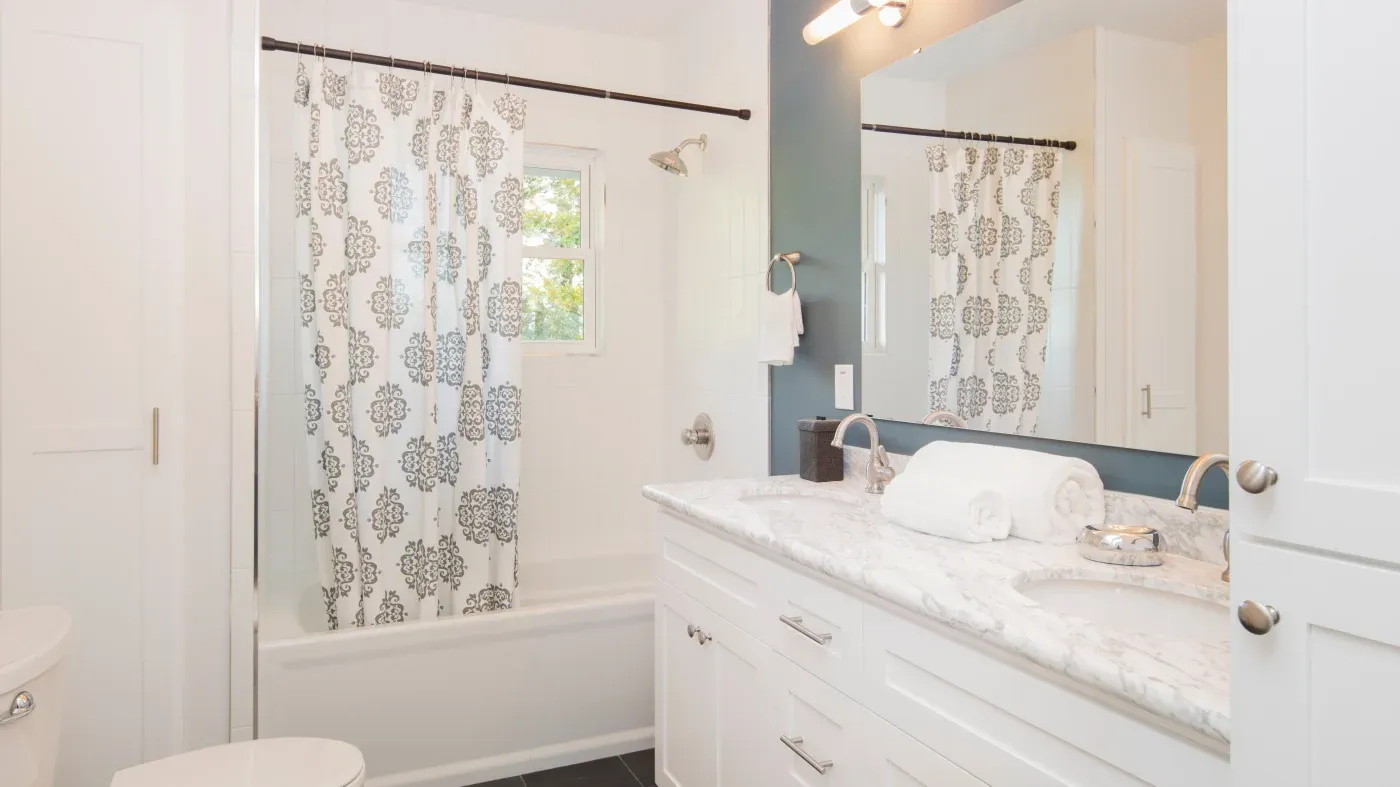 A bathroom with a white vanity, white tub, and detailed shower curtain