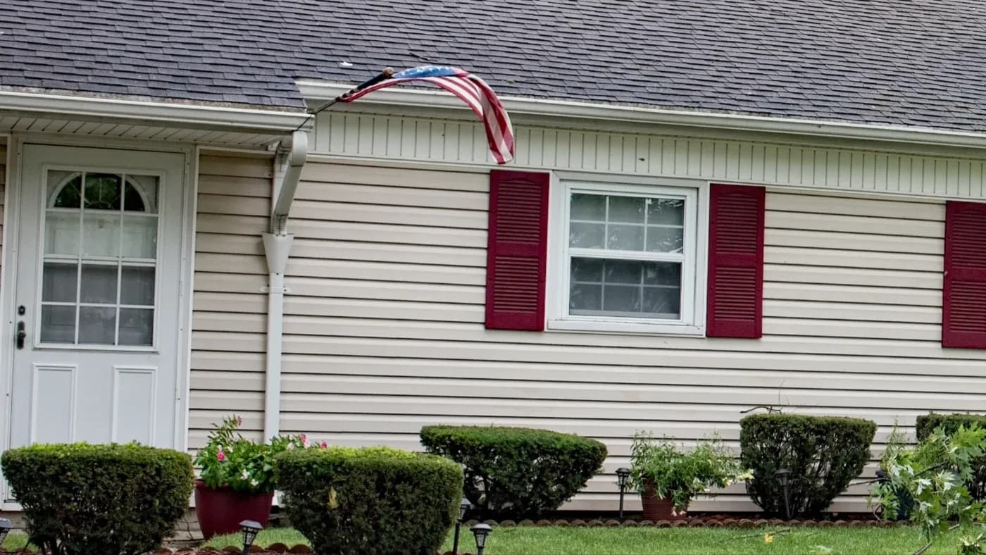 A home with beige siding and red shutters on white windows