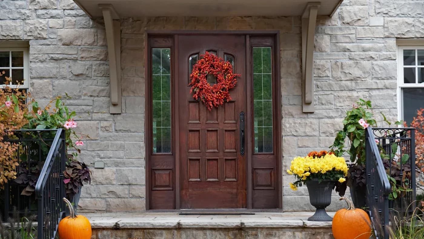 A brown door with glass panes and a red wreath in a home with stone siding